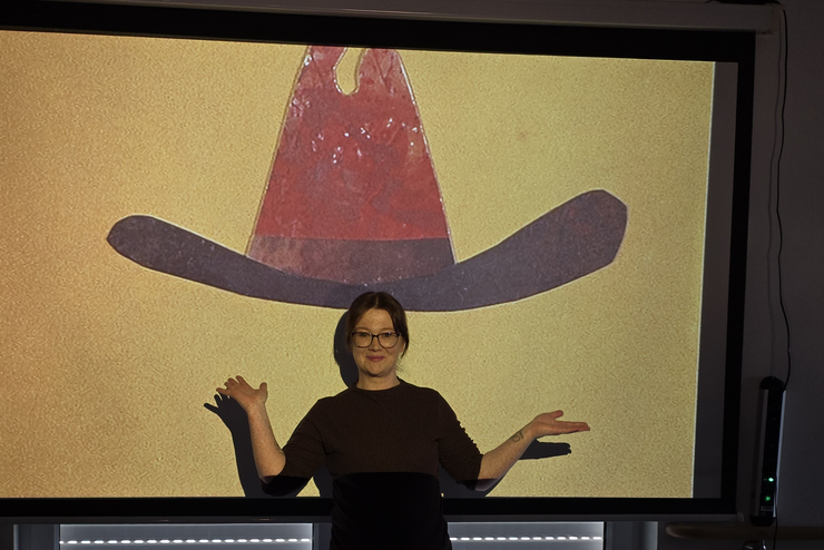 Eine Frau steht vor der Leinwand und auf der Leinwand ist ein Cowboyhut. Sieht so aus als ob die Frau die Hut aufhat.